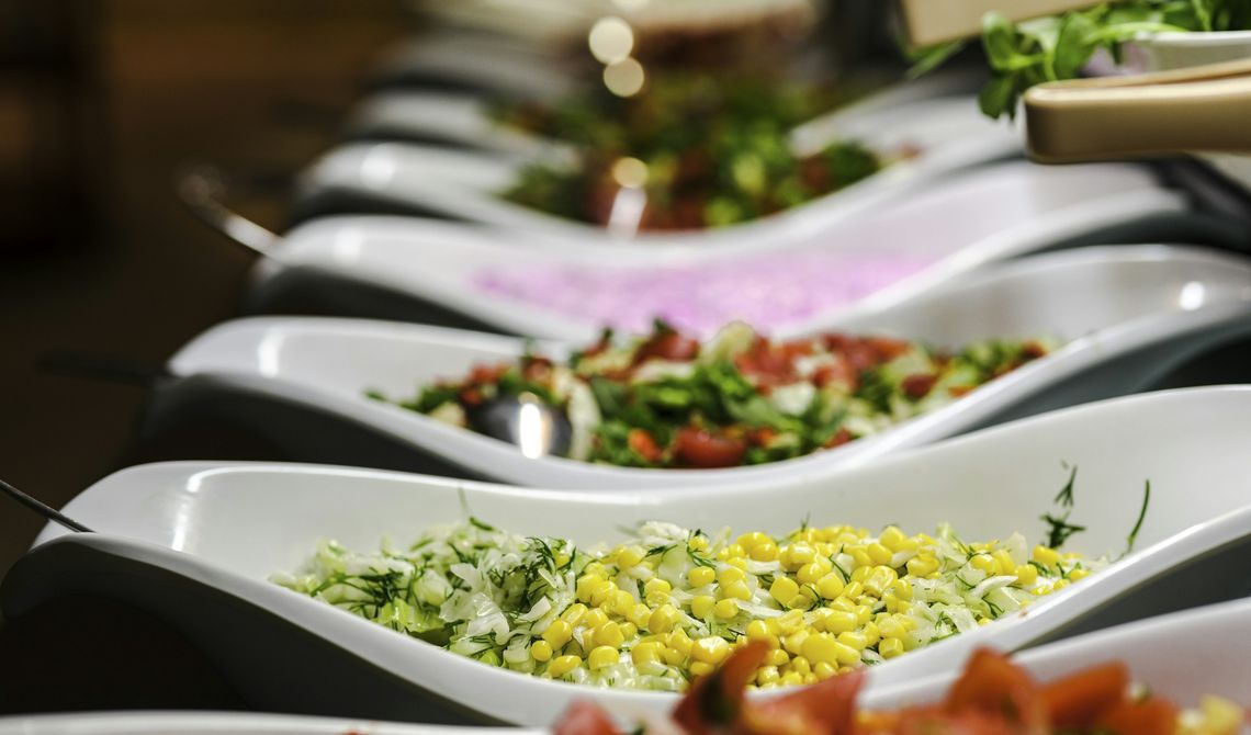 Fila de travessas brancas com saladas variadas