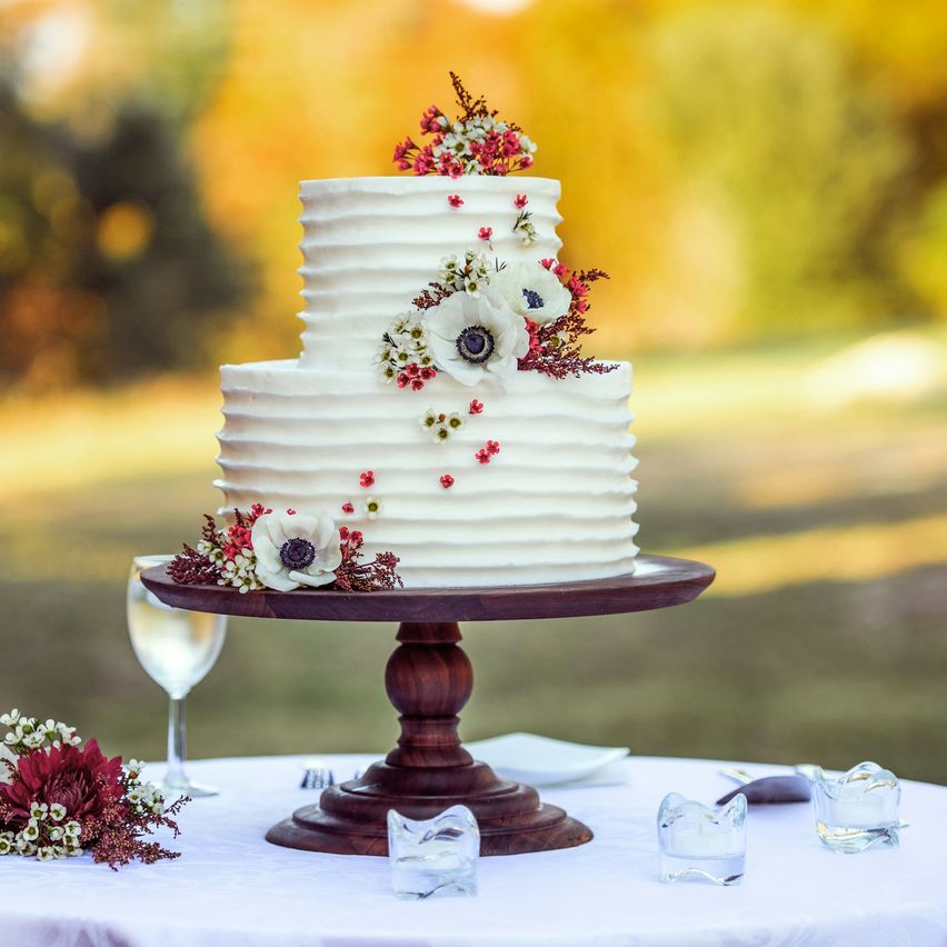 Bolo de noivos branco de dois andares, com flores, num prato de madeira
