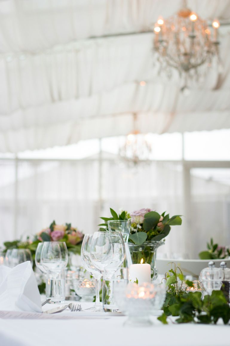 Mesa posta com velas e flores, sob uma tenda branca com lustres