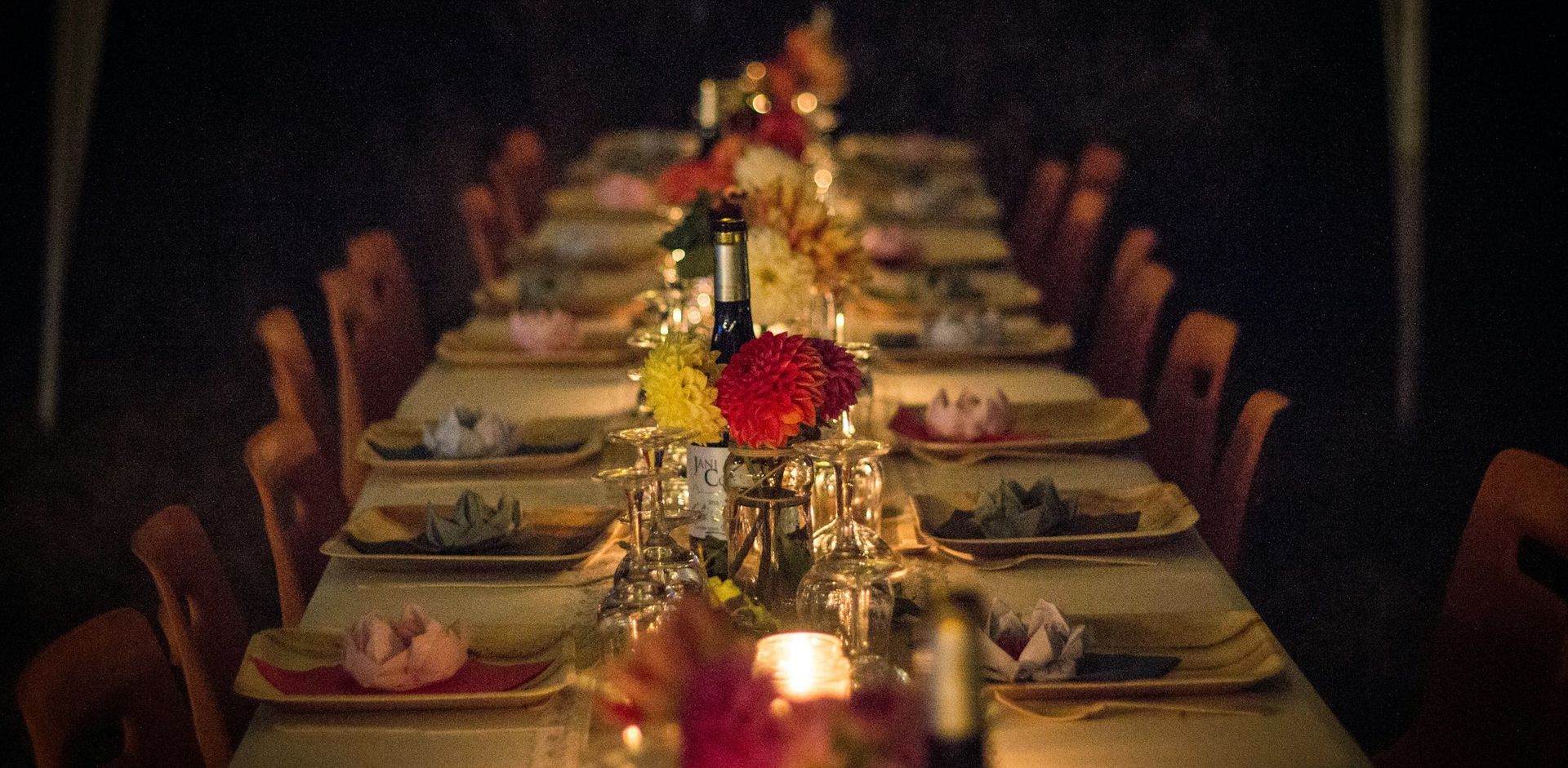 Mesa comprida posta para um jantar, com flores e velas