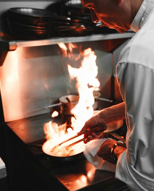 Cozinheiro a saltear numa frigideira, com chama alta