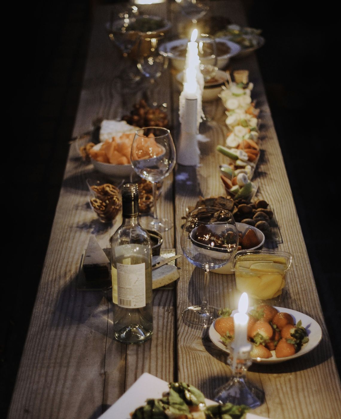 Mesa comprida de madeira posta para um jantar, com velas acesas