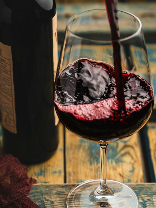 Vinho tinto a ser servido num copo, sobre uma mesa de madeira